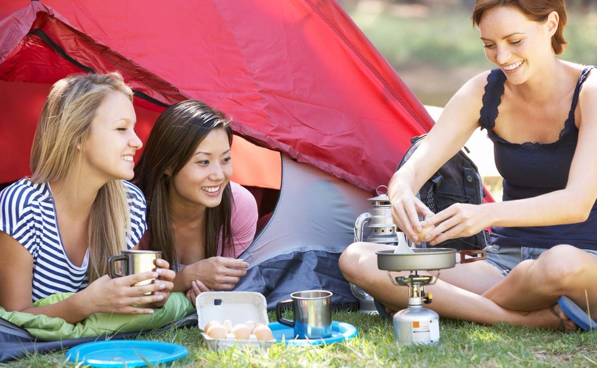 Three Young Women Cooking On Camping Stove Outside Tent