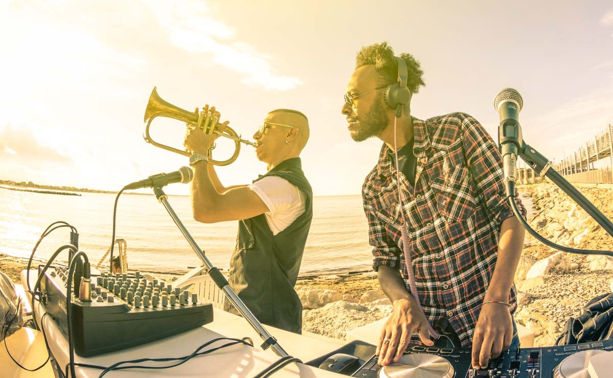 Trendy hipster dj playing summer hits at sunset beach party with