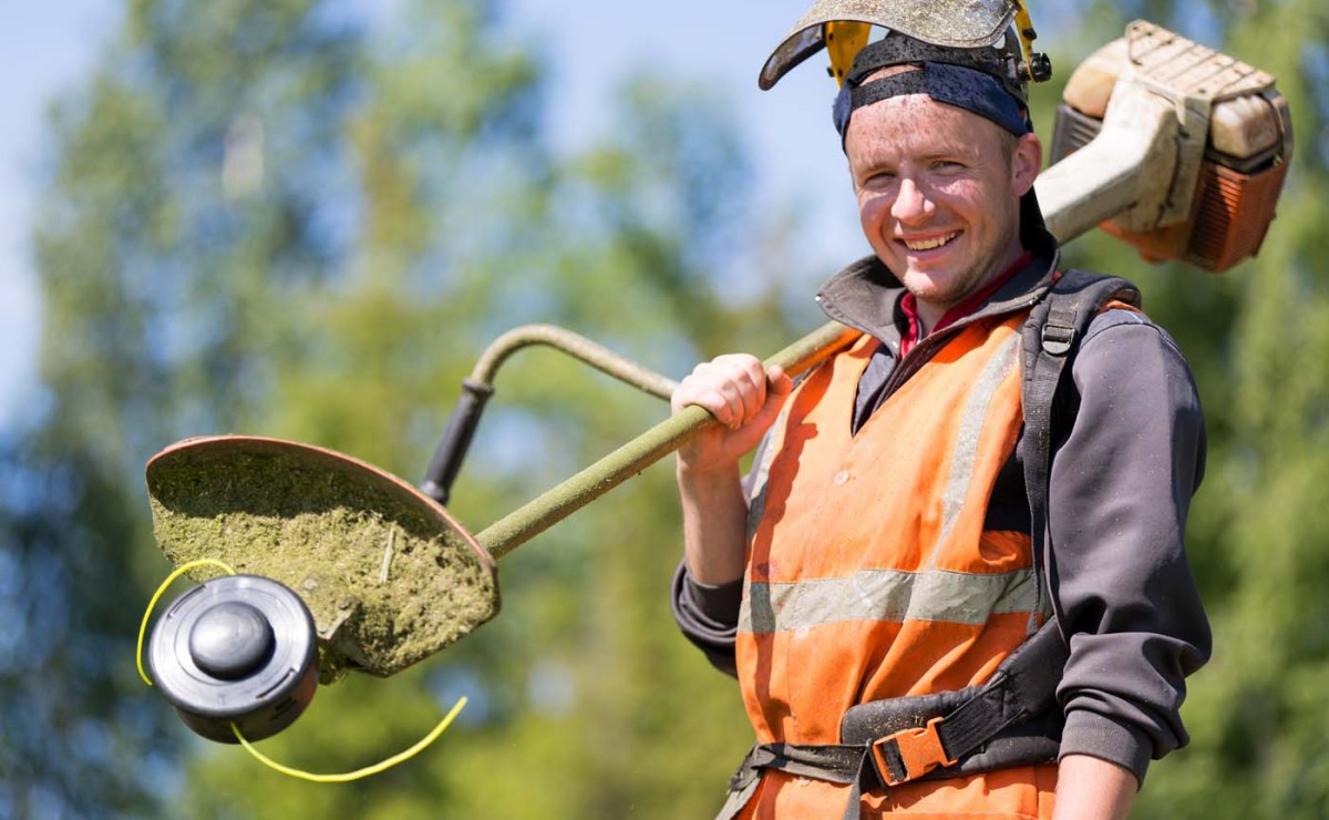 Portrait happy gardener man worker with gas grass trimmer equipm