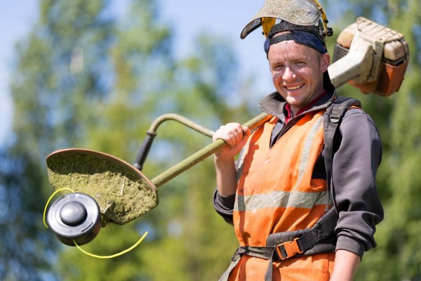 Portrait happy gardener man worker with gas grass trimmer equipm